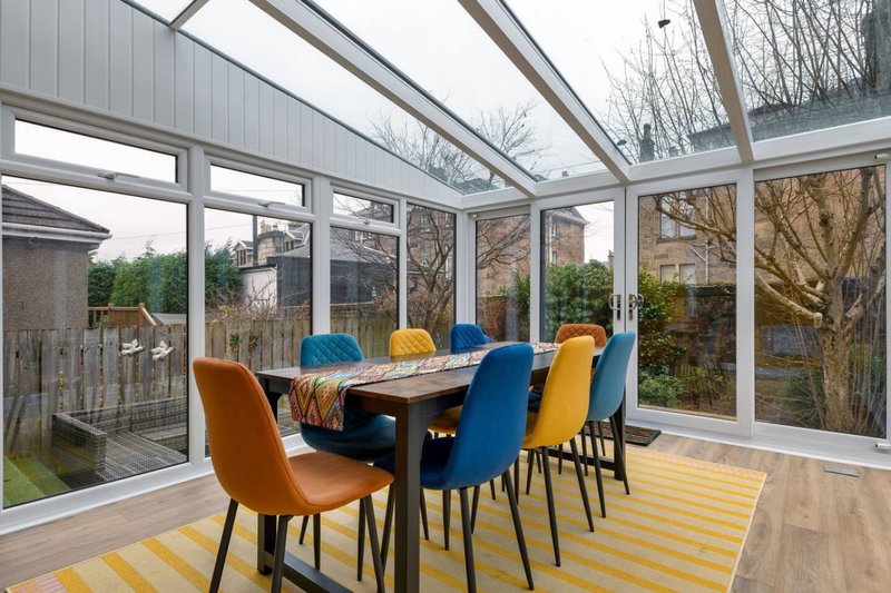 Modern conservatory with dining table, colorful chairs, and garden views through glass walls