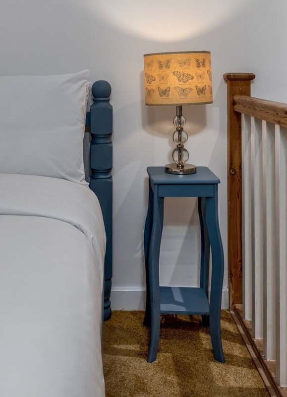 Bedroom corner with blue bedside table, lamp with patterned shade, and wooden crib