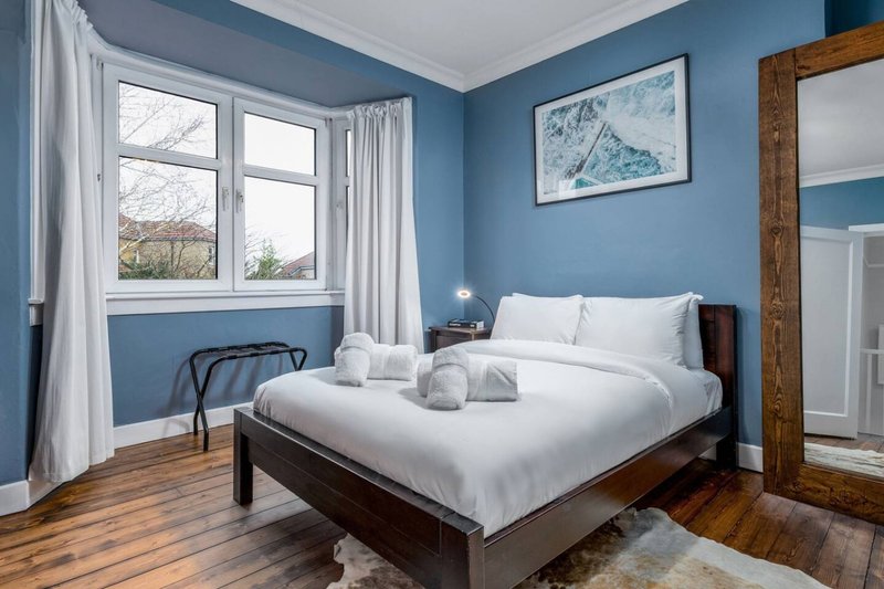 Bright bedroom with double bed, blue walls, wooden floor and large window