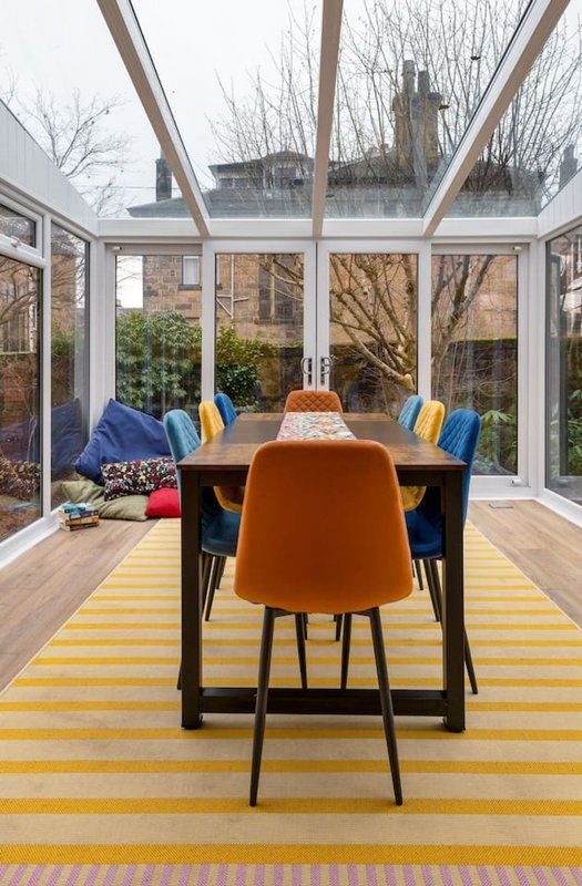 Modern dining room with orange chairs, wooden table, and glass conservatory overlooking garden
