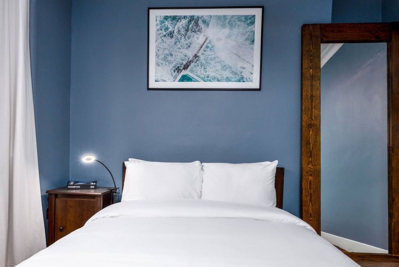 Modern bedroom with double bed, white bedding, blue-grey walls and framed coastal artwork