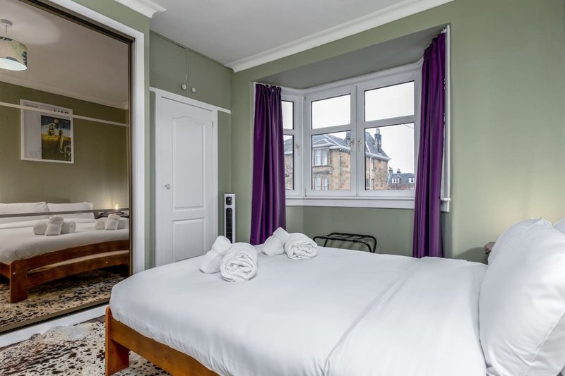 Bedroom with double bed, white bedding, purple curtains, and view of adjacent ensuite bathroom