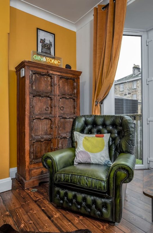 Bright yellow room with green leather armchair, wooden cabinet, and large window with curtains