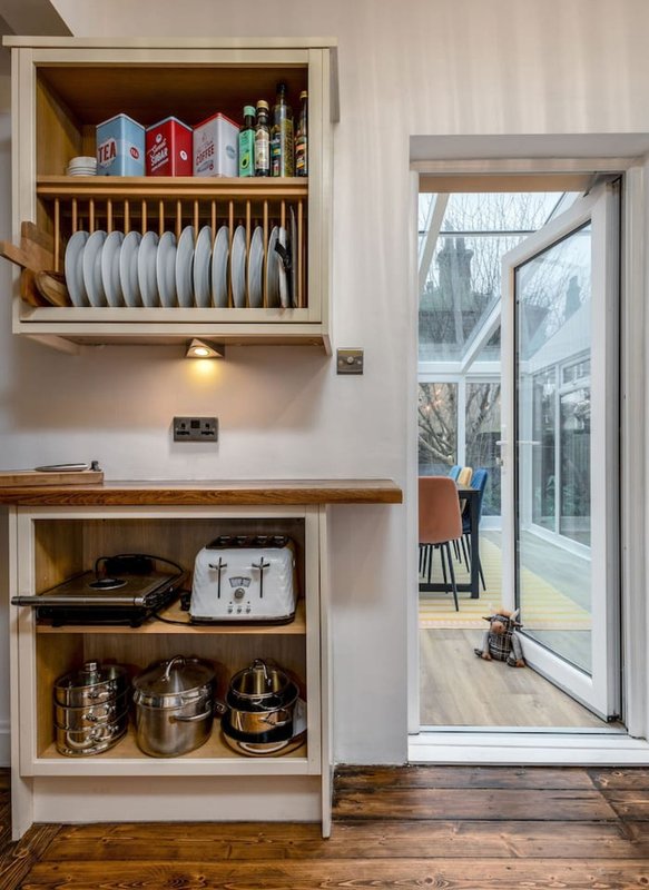 Kitchen shelving with plates, bowls, and cookware; glass door to garden visible