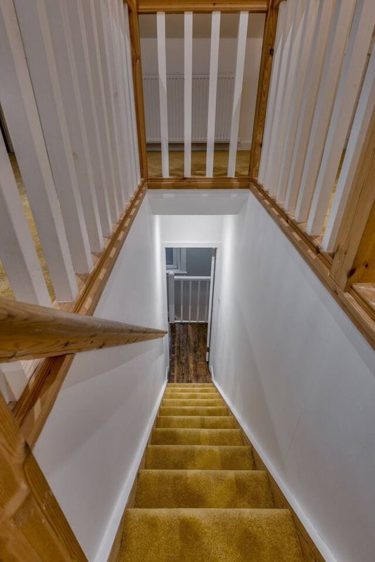 Wooden staircase with white walls and railings descending to lower level