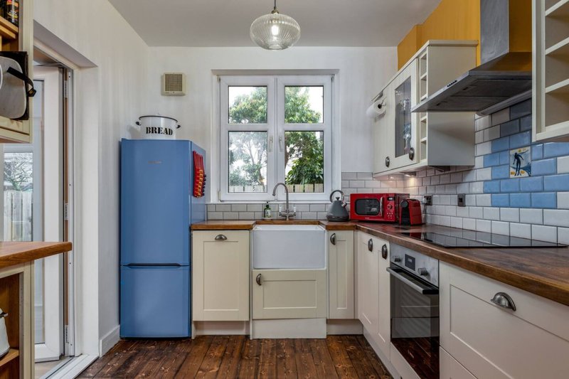 Bright galley kitchen with blue fridge, cream cabinets, white subway tile, and wooden worktops