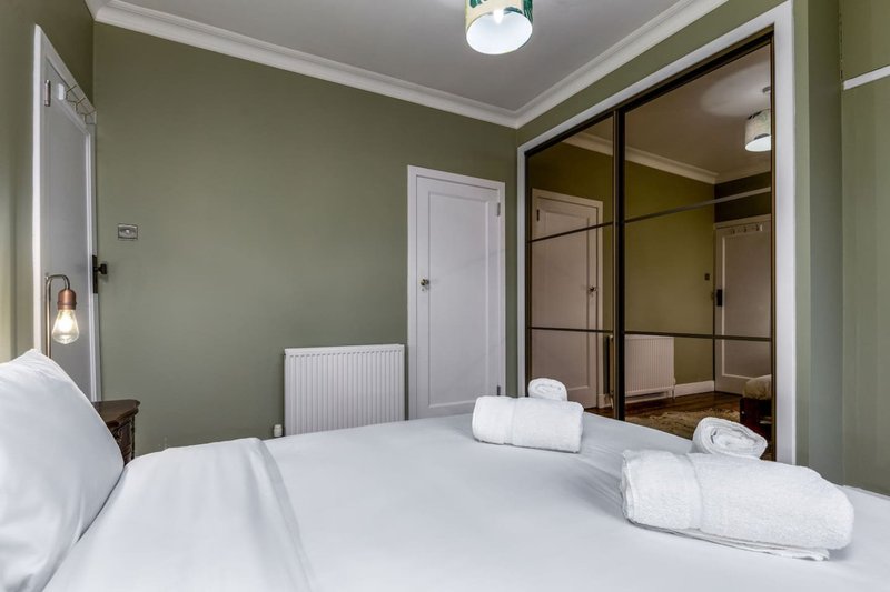 Modern bedroom with double bed, white bedding, sage green walls, and mirrored wardrobe