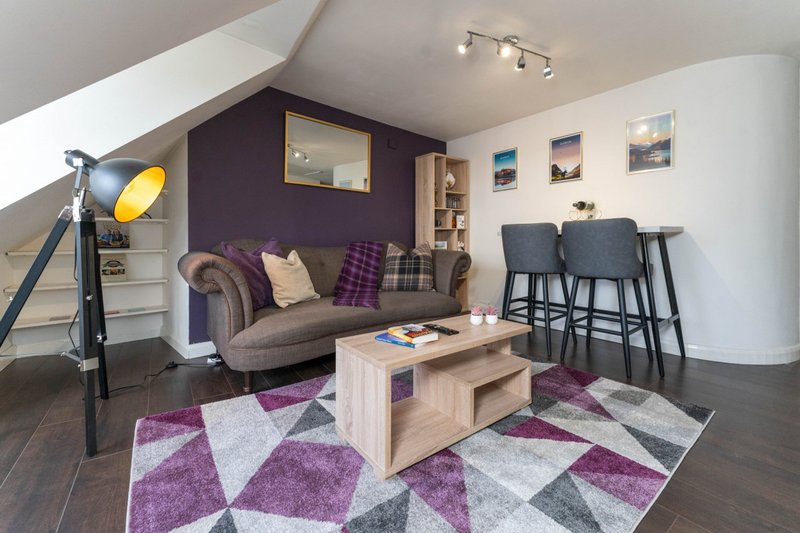 Modern open-plan living room with purple accent wall, sofa, dining area and geometric rug