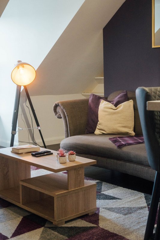 Attic bedroom with sloped ceiling, upholstered sofa, wooden coffee table and tripod lamp