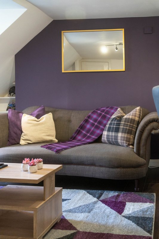 Attic living room with grey sofa, purple walls, patterned cushions and throws