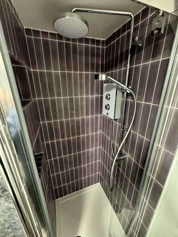 Modern shower enclosure with black tile walls, rainfall showerhead and chrome fixtures