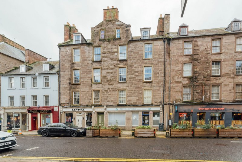 Stone tenement building with ground-floor shops and residential flats above, street view