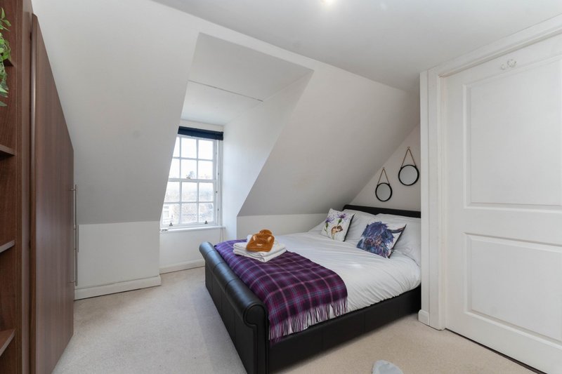 Bright attic bedroom with double bed, purple bedding, skylight window and white walls