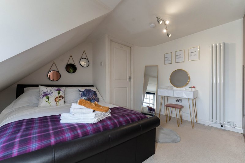 Bright attic bedroom with double bed, purple plaid blanket, desk, and decorative wall mirrors