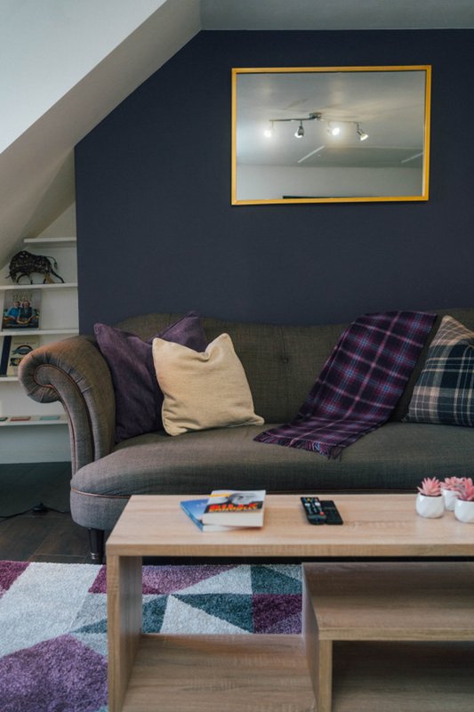 Attic living room with dark blue walls, grey sofa, purple and plaid cushions, wooden coffee table