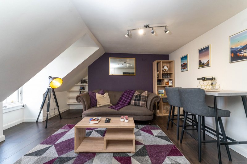 Attic living room with purple accent wall, sofa, wooden coffee table and desk area