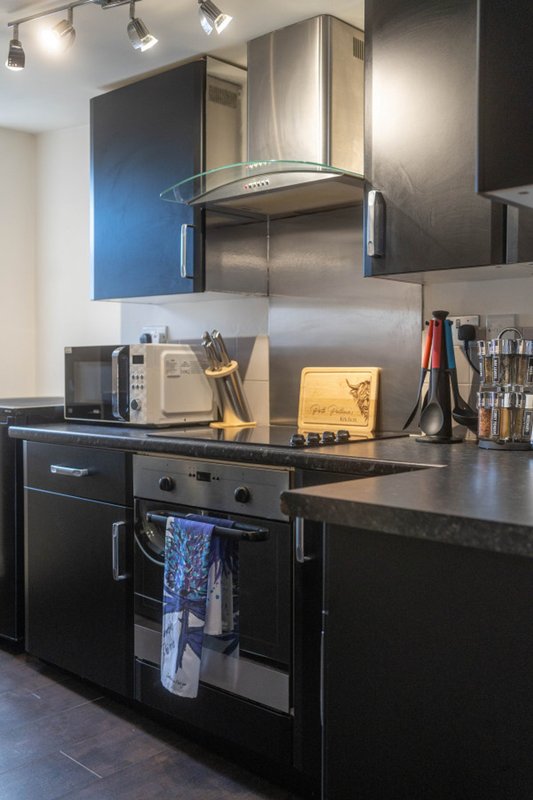 Modern kitchen with black cabinetry, stainless steel cooker hood, and granite countertops