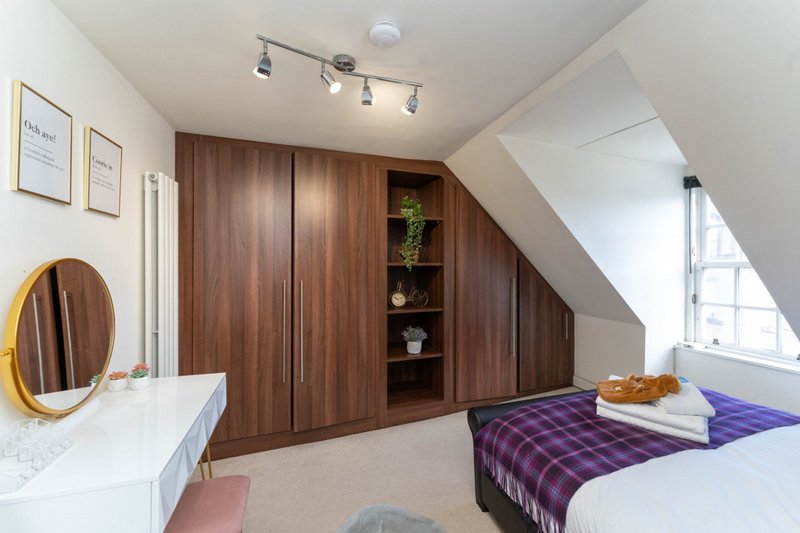 Bright attic bedroom with wooden wardrobe, double bed, round mirror and skylight window