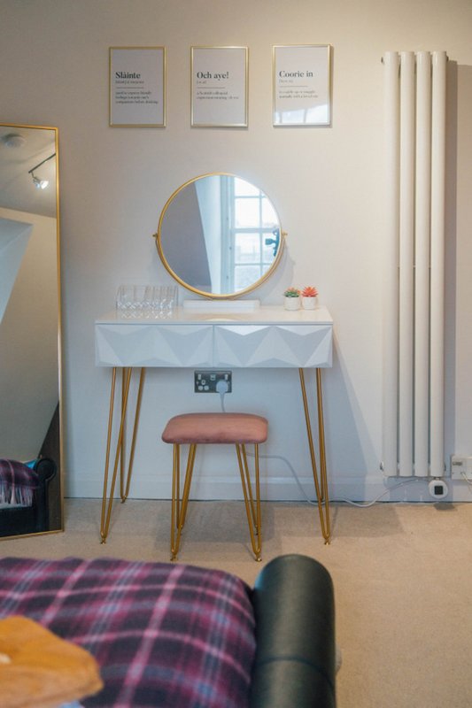 Bedroom dressing table with round mirror, wooden legs, stool, and framed wall art above