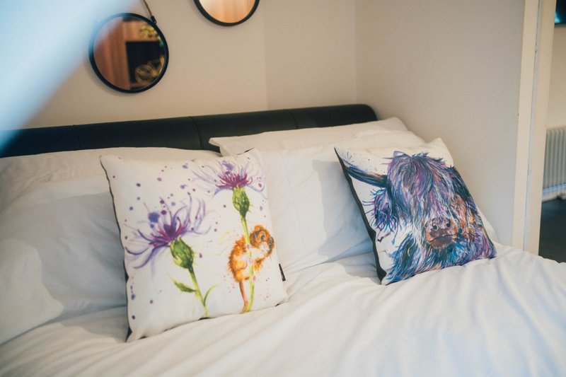 Bedroom with double bed, white bedding, decorative floral pillows and round wall mirrors