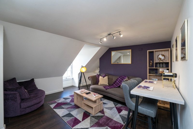 Attic living room with purple armchair, gray sofa, geometric rug and work desk