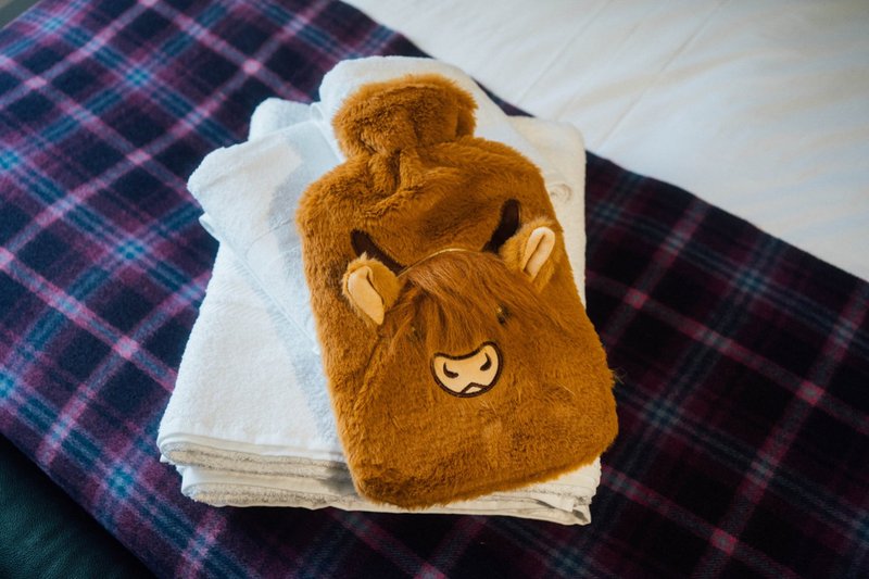 Brown plush hot water bottle with animal face on folded white and tartan blankets