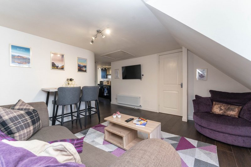 Attic studio with purple sofa, dining area, kitchenette and wall-mounted TV