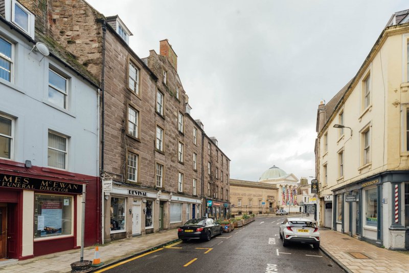 Street view of traditional stone buildings with shops and parked cars on residential high street