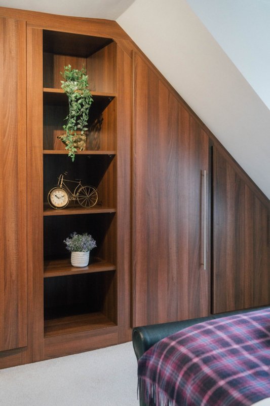 Bedroom alcove with wooden shelving, decorative plants, clock, and bed with plaid throw