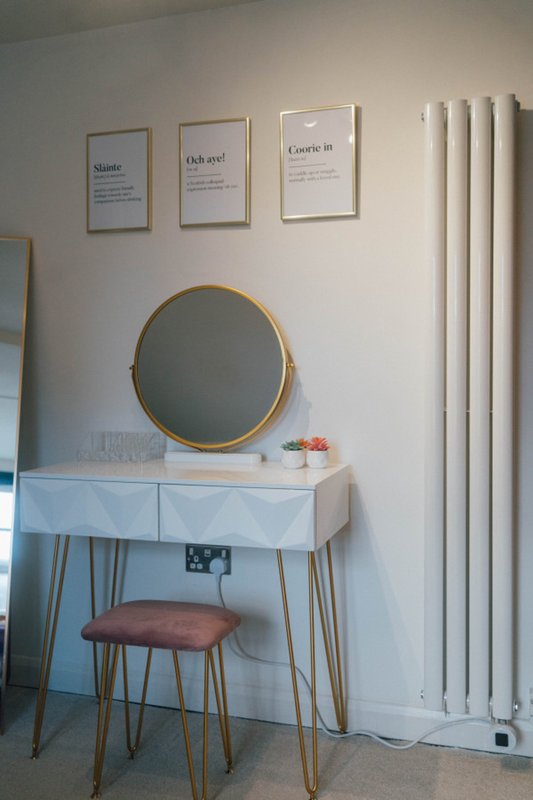 Bedroom dressing table with round mirror, wooden stool, and framed wall art above