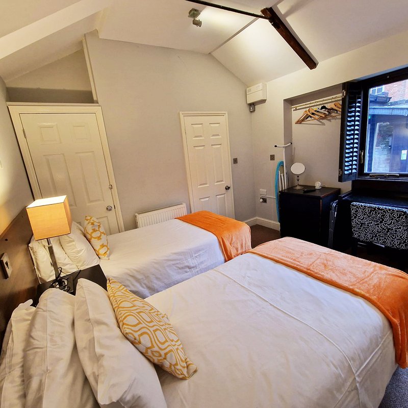 Bedroom with two twin beds, orange throws, bedside lamp, TV, and wooden beams