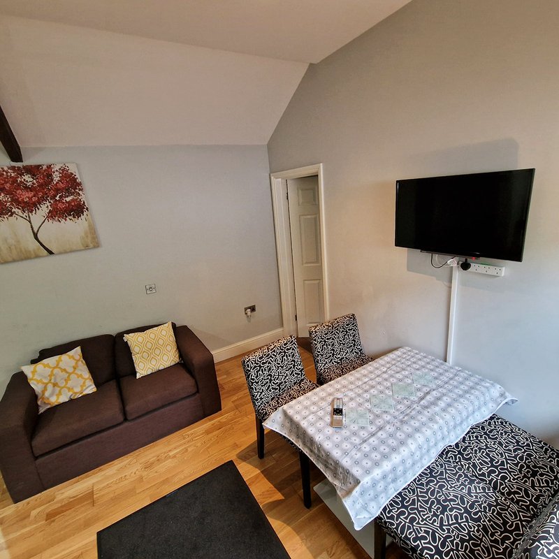 Studio apartment with brown sofa, dining table, wall-mounted TV and wooden flooring