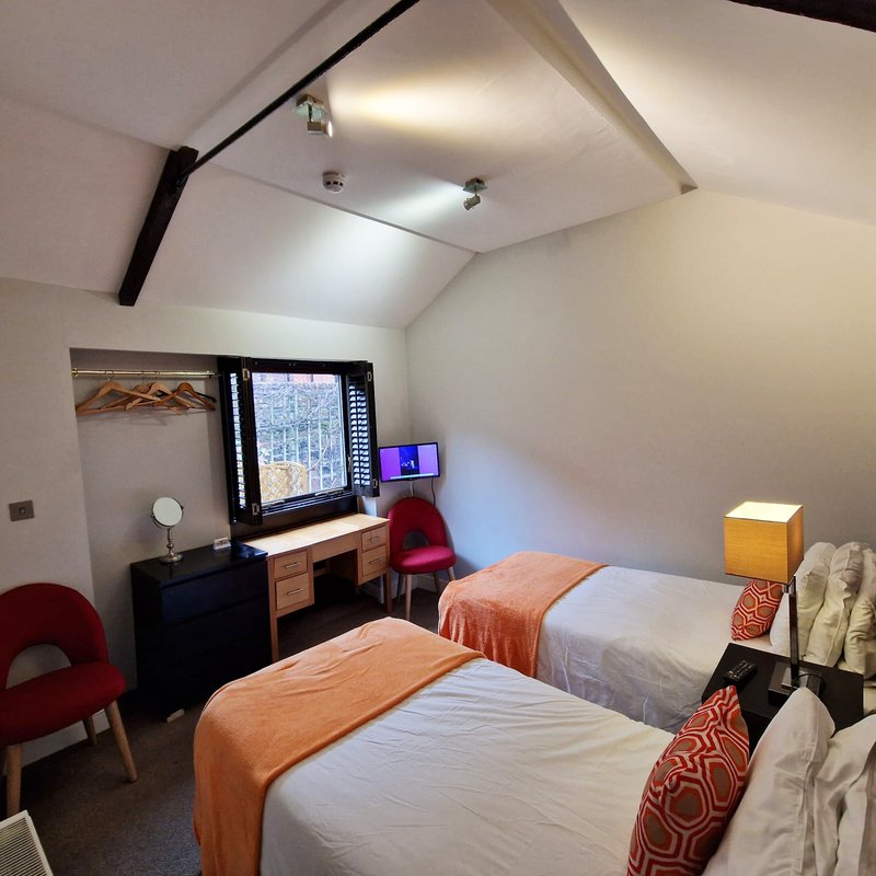Twin bedroom with sloped ceiling, two beds with orange throws, desk, window and red chair