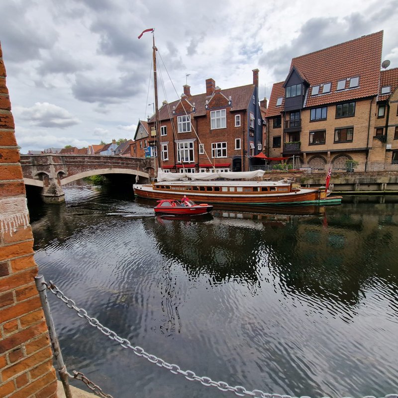 Riverside view of historic red-brick buildings with moored boat and bridge