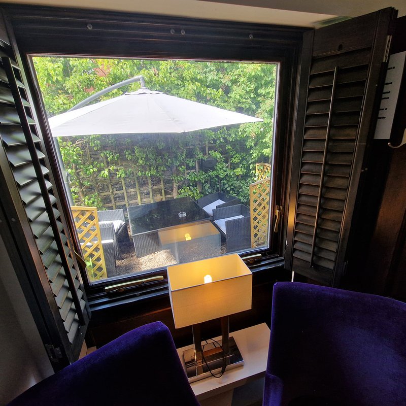 Interior view through large window to outdoor seating area with umbrella and garden