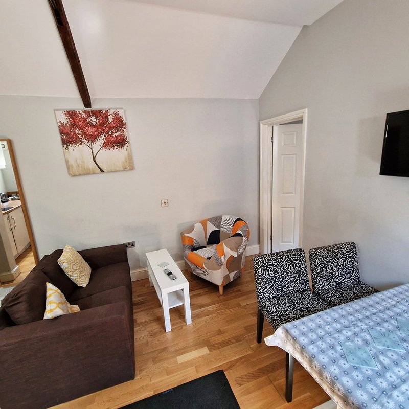 Studio bedroom with sofa, armchair, bed, wooden floor and wall art