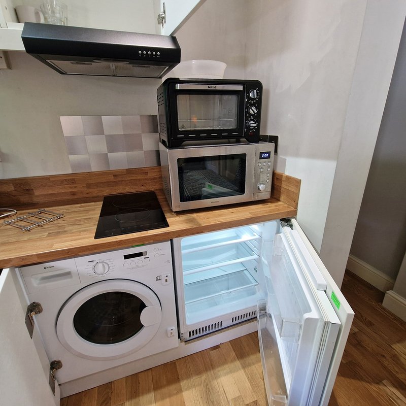 Compact kitchen with washing machine, microwave, oven, and refrigerator on wooden countertop