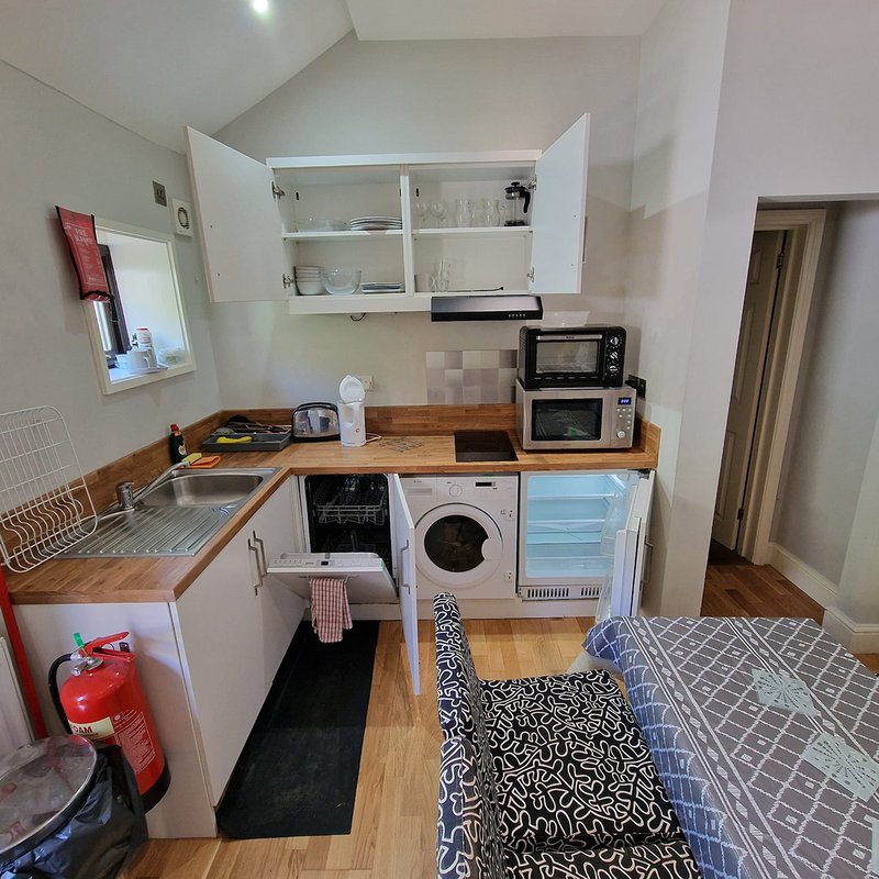 Compact kitchenette with white cabinets, wooden countertop, appliances and open shelving