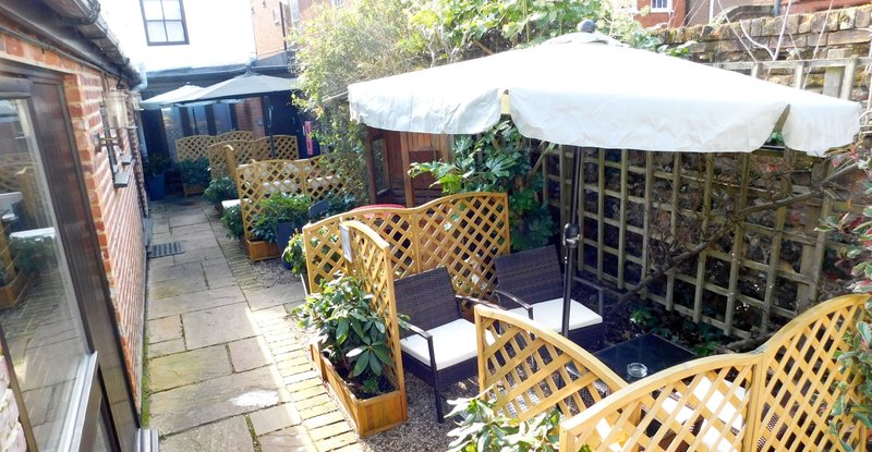 Paved garden patio with wooden lattice screens, potted plants, and white shade umbrellas
