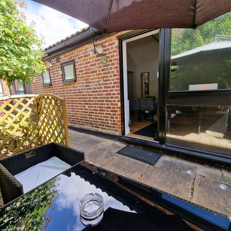 Brick cottage patio with umbrella, wicker chair, and glass doors to interior