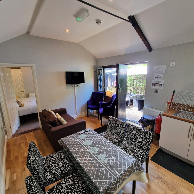 Open-plan living room with brown sofa, patterned rug, TV, wooden flooring and glass doors to garden
