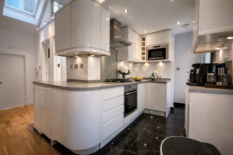 Modern kitchen with white cabinetry, black countertops, stainless steel appliances and skylight