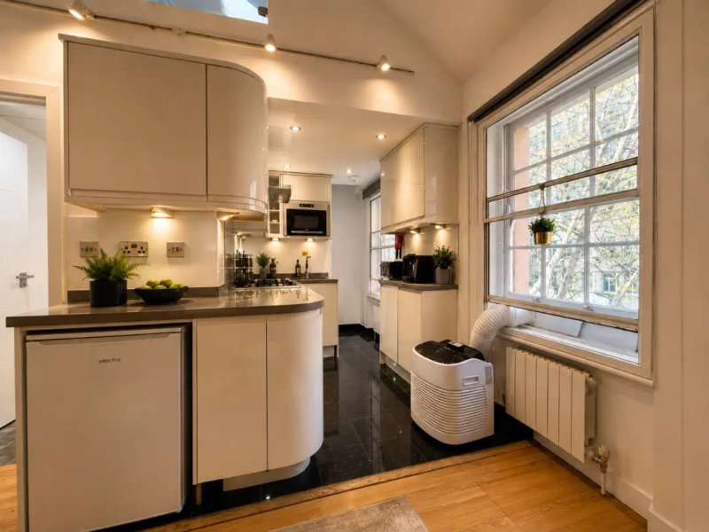 Modern kitchen with cream cabinetry, dark countertop, white appliances and large window