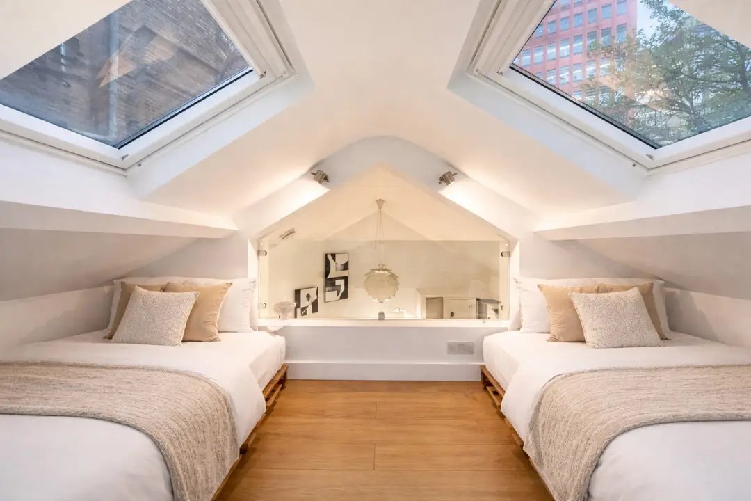 Bright attic bedroom with two single beds, skylights, wooden floor and built-in shelving