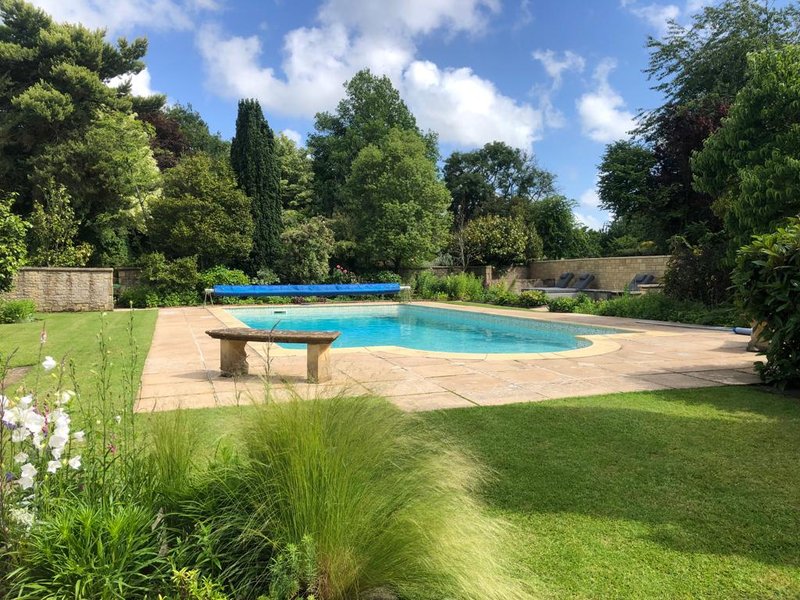 Swimming pool with surrounding garden, manicured lawn, stone patio and mature trees