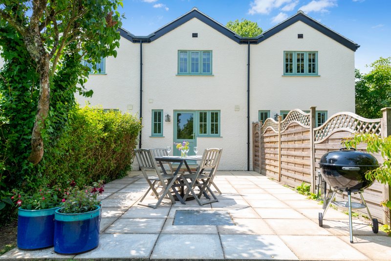 Modern white house with patio area, garden furniture, BBQ grill and wooden fence