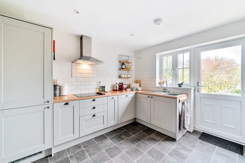 Modern white kitchen with subway tile backsplash, wooden countertops, and French doors to garden