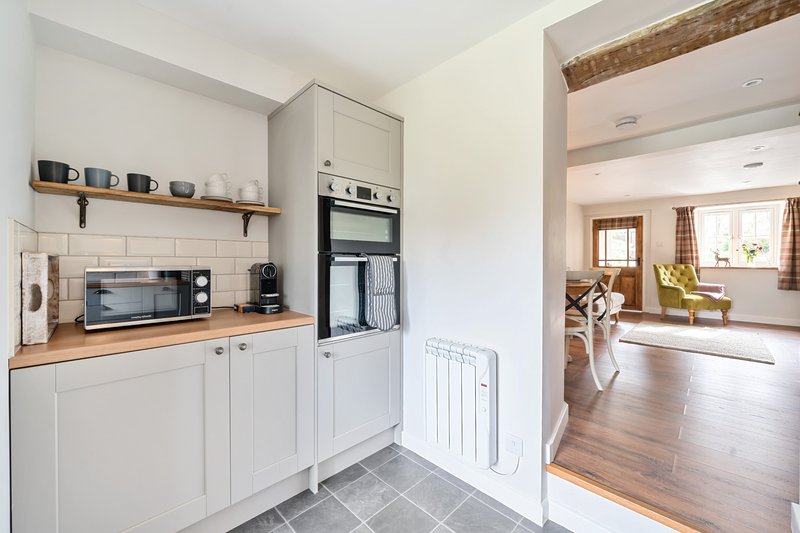Modern kitchen with white cabinetry, wooden countertop, built-in appliances and open view to living area