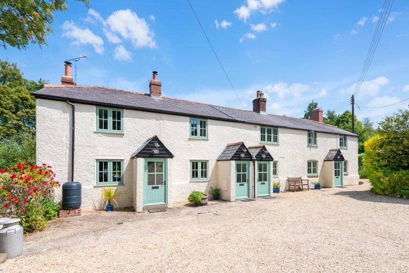 Whitewashed countryside cottage with multiple entrance doors, gravel driveway, and manicured garden