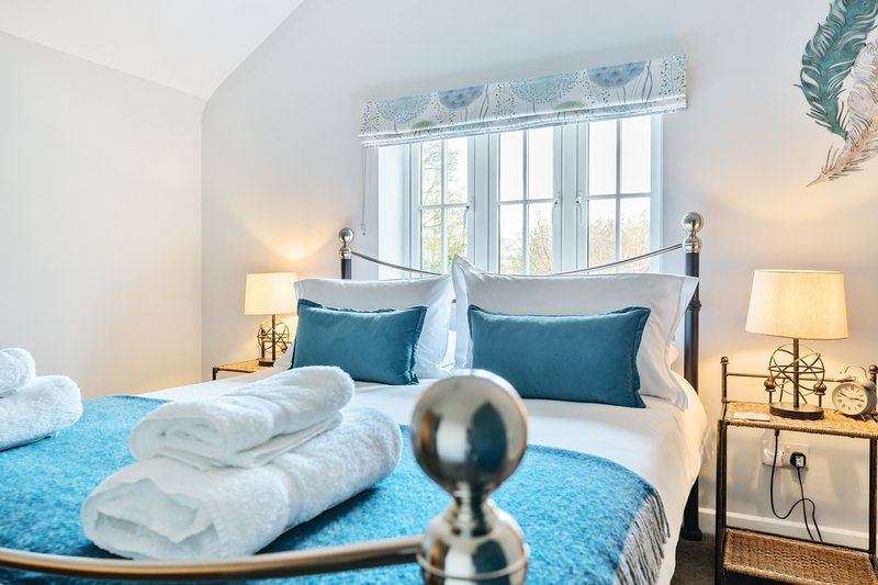 Bright bedroom with metal bed frame, blue bedding, white pillows, and side lamps
